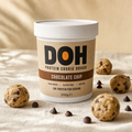 DOH Snacking Dough — Classic Chocolate Chip tub on warm cream linen with scattered cookie dough balls