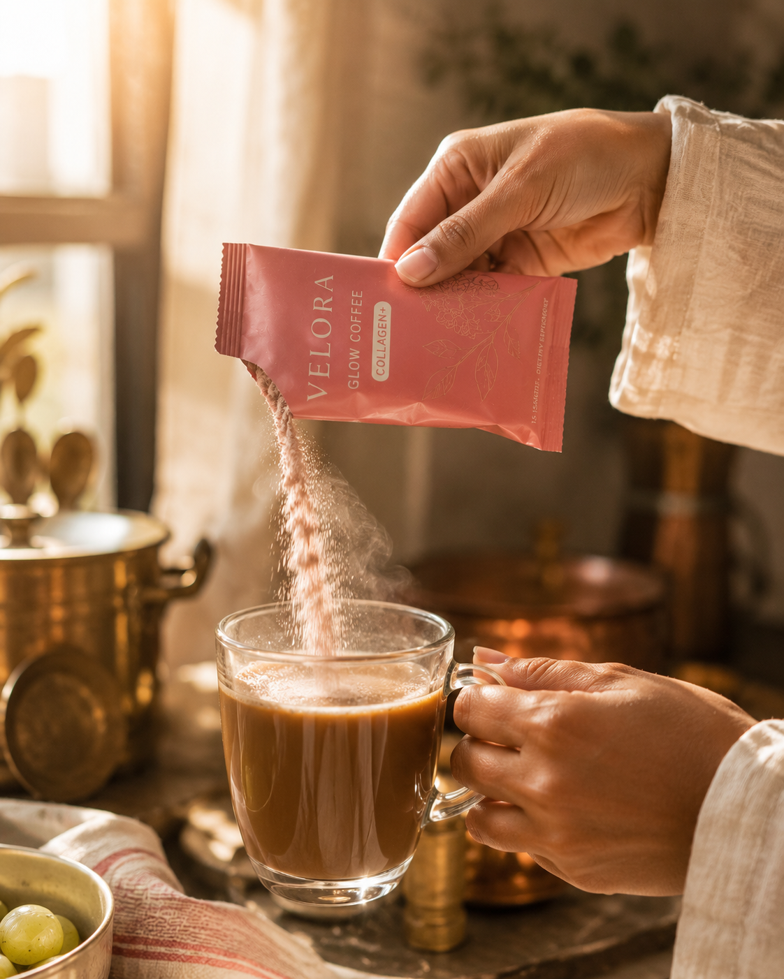 Pouring Velora Glow Coffee sachet into a glass mug, golden-hour kitchen with brass cookware